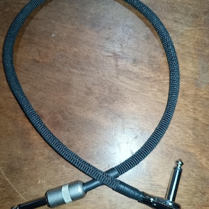 Peut inclure: Câble d'instrument noir avec une gaine en tissu tissé. Le câble a une prise jack droite de 0,635 cm à une extrémité et une prise jack coudée de 0,635 cm à l'autre extrémité. Les connecteurs sont argentés et noirs.