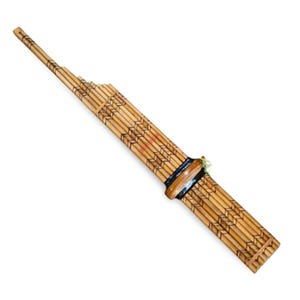 Könnte beinhalten: Ein traditionelles Bambus-Panflöteninstrument mit langem, schlankem Design. Das Instrument verfügt über eine Reihe von Bambuspfeifen unterschiedlicher Länge, die mit schwarzen Bändern und dekorativen Schnitzereien zusammengebunden sind. Die Panflöte hat eine hellbraune Farbe.
