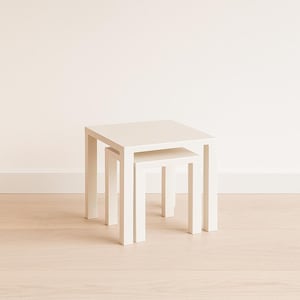 May include: Two white square nesting tables. The larger table is 18 inches wide and 18 inches deep, with a height of 18 inches. The smaller table is 12 inches wide, 12 inches deep, and 12 inches high. Both tables have a minimalist design.