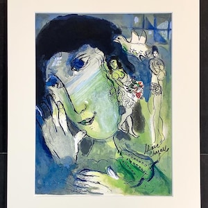 Pode incluir: Uma impressão de arte emoldurada com uma pintura surrealista com um rosto em tons de azul e verde. A obra de arte inclui figuras, uma pomba e a assinatura do artista. A impressão é emoldurada com uma borda branca.