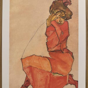 May include: A print of a seated figure in shades of red and orange, with a hand raised to the face. The artwork has a minimalist style, with visible brushstrokes and a muted color palette. The print is numbered 47/120 and signed by Egon Schiele.