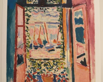 May include: A colorful print of a window overlooking a harbor with sailboats. The artwork features a vibrant palette of blues, pinks, and oranges, with visible brushstrokes. The artist's signature, Henri Matisse, is in the lower right corner.