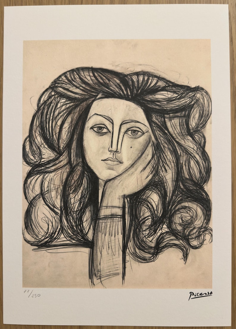 May include: Black and white sketch of a woman's face with long, flowing hair, resting her chin on her hand. The artwork is signed "Picasso" and numbered "77/250". The image has a vintage aesthetic.