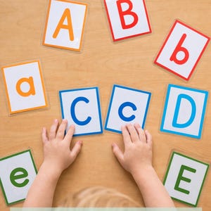May include: A set of rectangular educational cards featuring uppercase and lowercase letters of the alphabet in various colors including orange, red, blue, and green, arranged on a surface for matching practice.