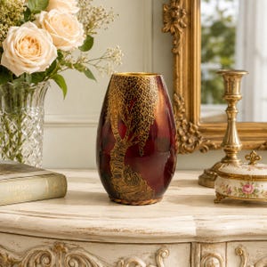 May include: A deep red, oval-shaped vase featuring a gold-toned, intricate tree design with textured bark and drooping branches. The vase has a smooth, glossy finish and a wide, open top, standing as a decorative piece on a flat surface.