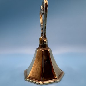 K&ouml;nnte beinhalten: Ein Messing-Kerzenhalter mit sechseckigem Sockel und einem ausgestellten, facettierten K&ouml;rper. Die Oberseite weist ein verziertes, gerolltes Design auf. Der Kerzenhalter hat eine warme, goldene Farbe und steht vor einem hellblauen Hintergrund.