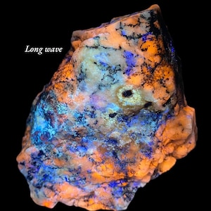 May include: A glowing rock formation with vibrant orange, blue, and black patterns. The text "Long wave" is visible in the upper left corner. The rock has a rough texture and is set against a black background, highlighting its unique colors.