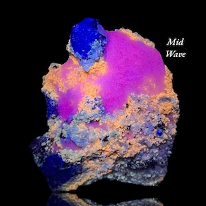 May include: A mineral specimen featuring vibrant patches of neon pink and deep blue crystalline structures interspersed with textured beige and tan mineral deposits. The text Mid Wave is printed in white on the upper right side of the specimen.