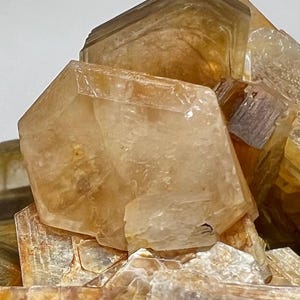 Puede incluir: Primer plano de un grupo de cristales translúcidos de color ámbar. Los cristales tienen una estructura geométrica en capas, con bordes afilados y una textura ligeramente rugosa. La apariencia general es natural y mineral.