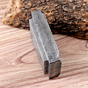 May include: A close-up view of a layered metal object with a distinctive, swirling pattern. The object has a textured surface and a dark, metallic colour. The design suggests a handcrafted or artisan product.