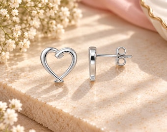 May include: A pair of silver-toned stud earrings featuring an open heart design. One earring is positioned to show the front heart shape, while the other is placed sideways to reveal the post and the circular butterfly clutch backing mechanism.