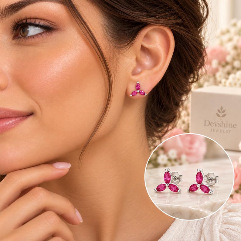 May include: A pair of silver stud earrings featuring three marquise-cut vibrant pink stones arranged in a floral cluster design. The earrings are shown worn on an earlobe and also displayed separately in a circular inset next to a Devshine Jewelry box.