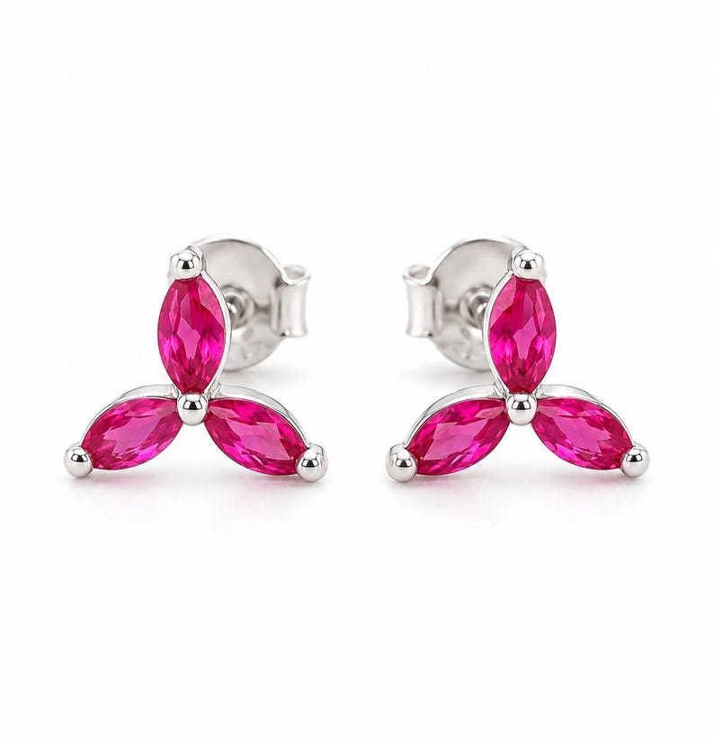 May include: A pair of stud earrings featuring three marquise-cut vibrant pink stones arranged in a clover-like cluster. The stones are set in a polished silver-toned metal frame, with each earring including a standard post and butterfly back closure.