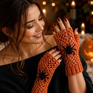 May include: A pair of orange fingerless gloves featuring a crocheted openwork pattern and a black spider appliqué on each glove. The gloves have a ribbed cuff at the wrist and extend to cover the back of the hand, leaving the fingers exposed.