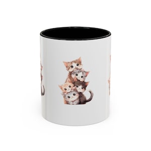 May include: White ceramic mug with a black interior. The mug displays a watercolour illustration of five kittens, stacked on top of each other. The kittens are in shades of brown, grey, and cream, with large eyes.