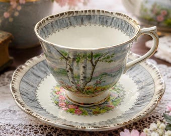Può includere: Servizio da tè in porcellana. La tazza e il piattino presentano un motivo marmorizzato blu chiaro e bianco con bordi dorati. La tazza presenta una scena paesaggistica con alberi. Il piattino ha un motivo floreale al centro.