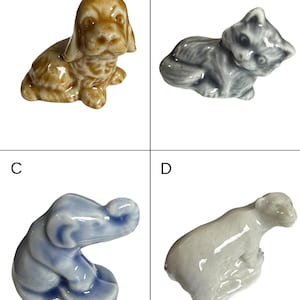 May include: Four small ceramic animal figurines: a tan dog, a gray cat, a blue elephant, and a white bear. Each figurine is detailed and appears to be hand-painted, showcasing a glossy finish. The animals are in various poses.