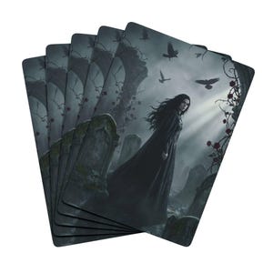May include: A stack of playing cards featuring a gothic illustration. The artwork depicts a woman in a black dress in a graveyard, with crows flying overhead. The background includes tombstones, arches, and rose vines.