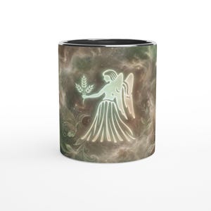 May include: White ceramic mug featuring a Virgo zodiac design. The design depicts a glowing figure holding wheat, set against a nebula-like background with green and brown tones. The mug has a black rim.