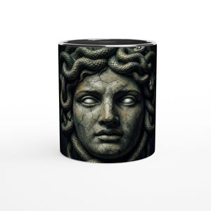 Könnte beinhalten: Keramik-Kaffeetasse mit einer detaillierten Illustration des Gesichts der Medusa. Das Design zeigt eine steinartige Textur mit Schlangen als Haare sowie einen schwarzen Innenraum und Rand. Die Tasse hat eine Standardgröße.
