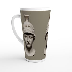 May include: A tall white ceramic latte mug featuring a repeating graphic print of a classical marble bust of a figure wearing a crested helmet. The design is set against a solid taupe background, with a curved handle on the left side of the mug.