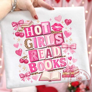 May include: White t-shirt with a pink and leopard print design. The text "HOT GIRLS READ BOOKS" is displayed in pink block letters. The design includes pink hearts, bows, cherries, and books.