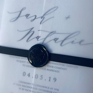 May include: A translucent vellum wedding invitation featuring the names Sash + Natalie in elegant script, secured with a black ribbed ribbon and a circular black wax seal embossed with a botanical leaf design, displaying event details and the date 04.05.19.