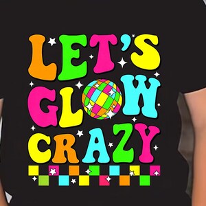 May include: A black t-shirt with the text "LET'S GLOW CRAZY" in vibrant, retro-style lettering. The design includes a colorful disco ball graphic and a checkered border. The child is wearing black sunglasses.