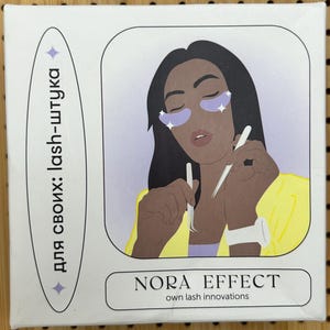 May include: A white box with a stylized illustration of a person with eye patches and holding tools. The box has the text "NORA EFFECT own lash innovations" and text in a vertical oval shape.
