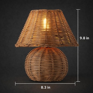 Handwoven wicker table lamp with natural rattan base and matching woven lampshade shown with size reference measurements of approximately 9.8 inches in height and 8.3 inches in width. The organic texture and handcrafted appearance create a warm and natural aesthetic. This decorative lamp provides soft ambient lighting and works beautifully in boho, rustic, coastal, or Scandinavian interior spaces. Perfect for bedside tables, living rooms, or cozy corners.