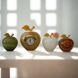May include: Four decorative apple-shaped objects. One is a green stone, another is a clock with a gold-colored frame and hands, and the other two are white and brown stone. All have gold-colored leaf accents.