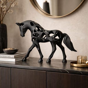 May include: A black, openwork horse sculpture. The decorative piece has a sleek, modern design with cut-out details. It stands on a dark surface, with a blurred background including a mirror and other decor. The horse is a decorative home accent.