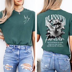 May include: Teal short-sleeved t-shirt with a white dove graphic on the front. The back of the shirt features the words "Blessed Forever" above a dove and floral design, with a scripture quote below.