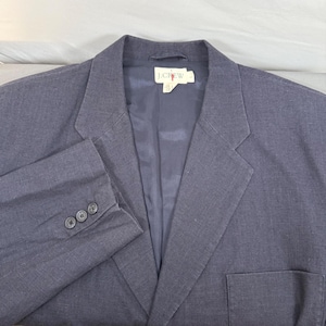 May include: A dark blue blazer with a notched lapel, a chest pocket, and three buttons on each cuff. The blazer has the "J.CREW" label on the inside. The fabric appears to be a woven material.