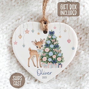 May include: Heart-shaped Christmas ornament with a deer and Christmas tree design. The ornament features a deer with a blue bow, a decorated tree, and the name "Oliver" with the year "2025". Includes a "Gift Box Included" tag.