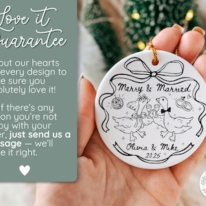 May include: White ceramic ornament with a black and white illustration of two geese toasting with champagne glasses, a disco ball, and wedding rings. The text "Merry & Married" and names "Olivia & Mike 2025" are also included.