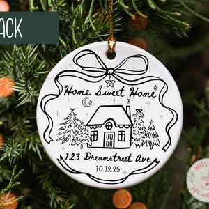 May include: White ceramic Christmas ornament with a black line drawing of a house, trees, and the text "Home Sweet Home." Includes the address "123 Dreamstreet Ave" and the date "10.12.25." A black banner at the top reads "BLACK."