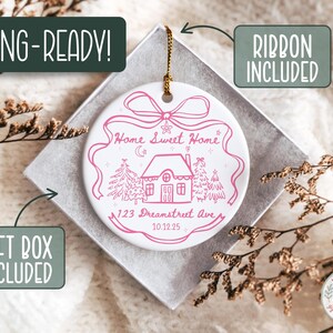 May include: White ceramic ornament with a pink house design, text reading "Home Sweet Home" and "123 Dreamstreet Ave 10.12.25". Includes a gold ribbon for hanging. Comes in a gift box.