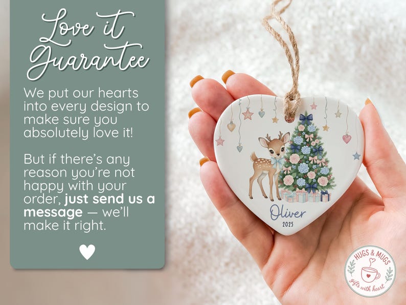 May include: Heart-shaped ceramic ornament featuring a fawn and Christmas tree design. The ornament has a string for hanging and includes the name "Oliver" and the year "2025". The ornament is held in a hand.