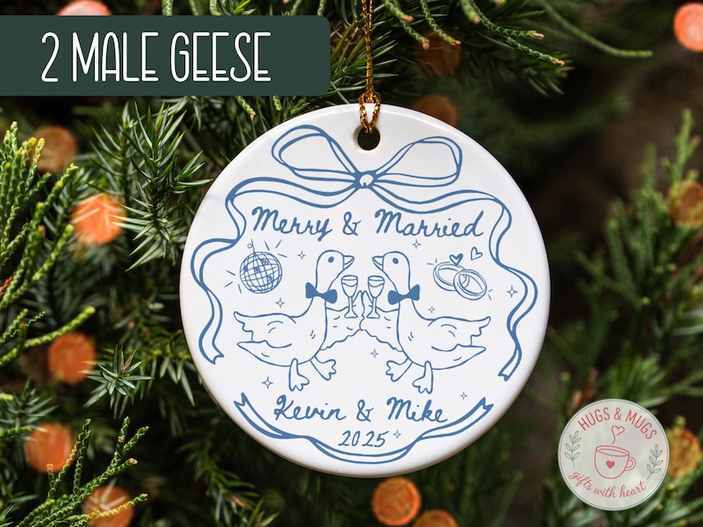 May include: A white ceramic ornament with a blue illustration of two geese toasting with champagne glasses. The ornament has the text "Merry & Married", "Kevin & Mike", and the year "2025". The top of the ornament has a hole for hanging.