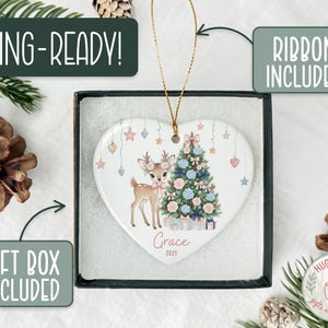 May include: Heart-shaped Christmas ornament featuring a deer and Christmas tree design. The ornament is in a gift box with a ribbon. Text on the ornament reads "Grace 2025". The packaging includes the text "GIFTING-READY!" and "GIFT BOX INCLUDED".