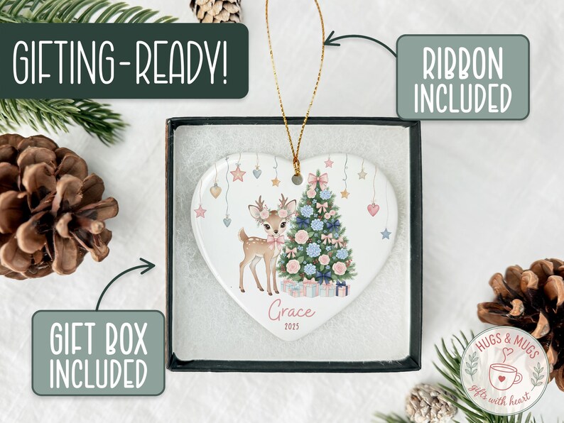 May include: Heart-shaped Christmas ornament featuring a deer and Christmas tree design. The ornament is in a gift box with a ribbon. Text on the ornament reads "Grace 2025". The packaging includes the text "GIFTING-READY!" and "GIFT BOX INCLUDED".