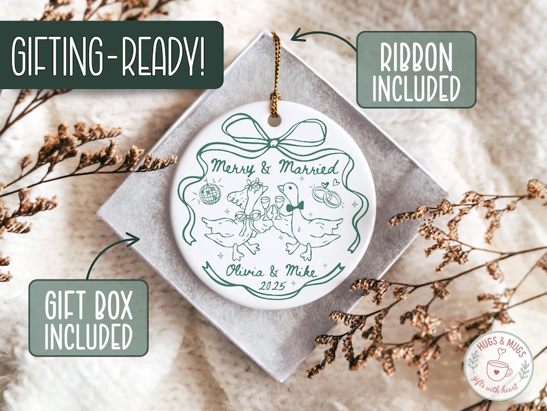May include: White ceramic wedding ornament with a green illustration of two geese toasting with champagne glasses. The ornament reads "Merry & Married", "Olivia & Mike 2025", and includes a gift box and ribbon. The ornament is ready for gifting.