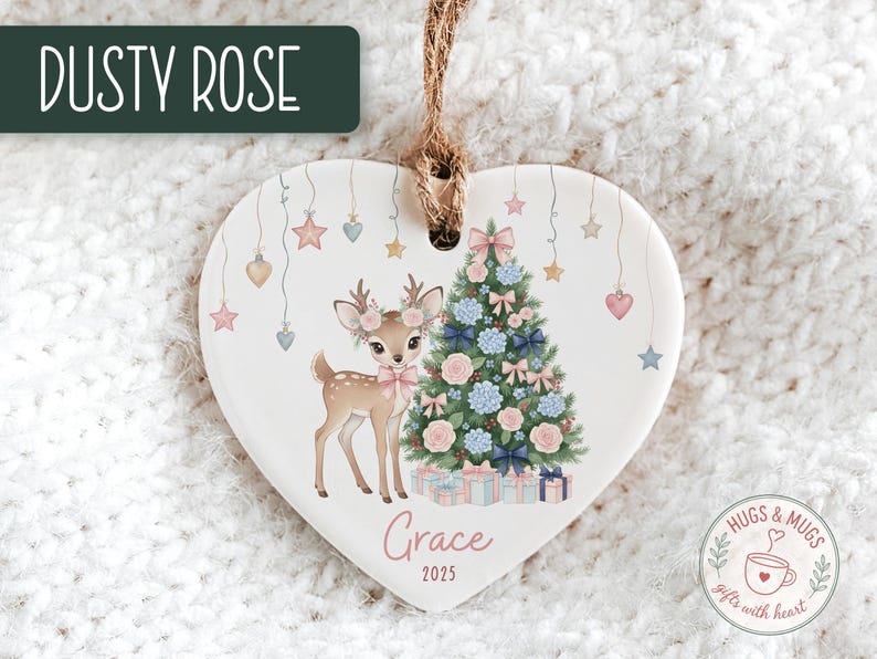 May include: Heart-shaped Christmas ornament with a deer and Christmas tree design. The ornament features a deer with floral antlers and a pink bow, a decorated tree, and the name "Grace" with the year 2025. The text "Dusty Rose" is at the top.