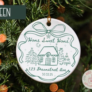 May include: White ceramic Christmas ornament with a green illustration of a house, trees, and the text "Home Sweet Home" and "123 Dreamstreet Ave 10.12.25". The word "GREEN" is in a green rectangle at the top.