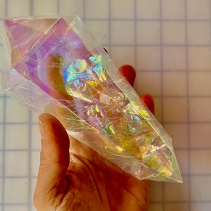 May include: A large iridescent clear crystal shaped like a point. The crystal has a rainbow effect and is held in a hand.