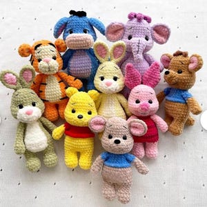Peut inclure: Collection de peluches crochetées à la main, aux couleurs vives. Les personnages incluent un ours jaune, un cochon rose, un lapin vert, un âne bleu, un éléphant violet et un ours brun, tous avec des détails.