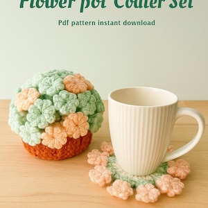 May include: A crochet flower pot coaster set with a matching coaster and a white mug. The set features a flower pot design with green, orange, and peach-colored flowers. The text "Flower pot Coaster Set" is displayed.