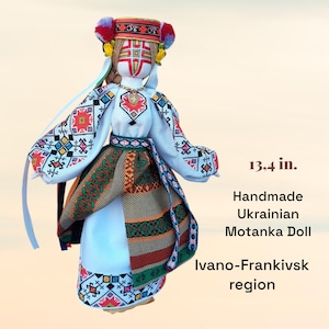 May include: Handmade Ukrainian Motanka doll, 13.4 in. tall, with a white embroidered blouse, colorful skirt, and a decorative headpiece. The doll's face is painted with traditional patterns. The text says "Ivano-Frankivsk region".