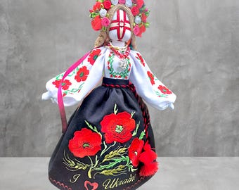 May include: A handmade doll in traditional Ukrainian attire. The doll features a white blouse with red floral embroidery, a black skirt with large red poppy embroidery, and a floral headdress. The text "I ❤️ Ukraine" is embroidered on the skirt.